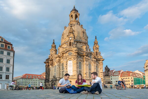 Three students are sitting on the front area of Frauenkirche and discussing.