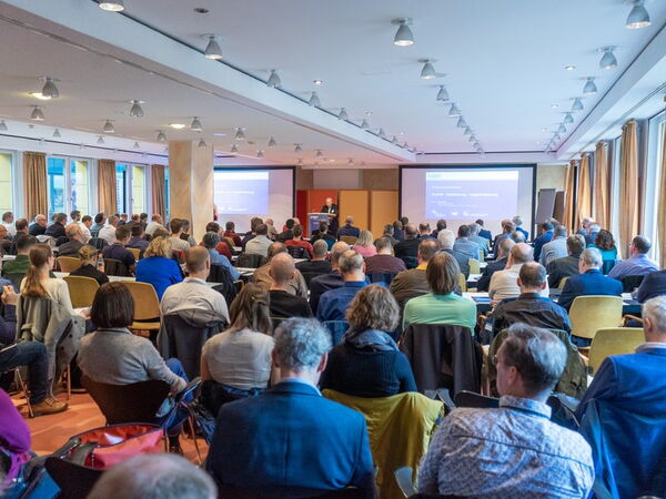 Many people are sitting in a seminar room and listening to the speaker.