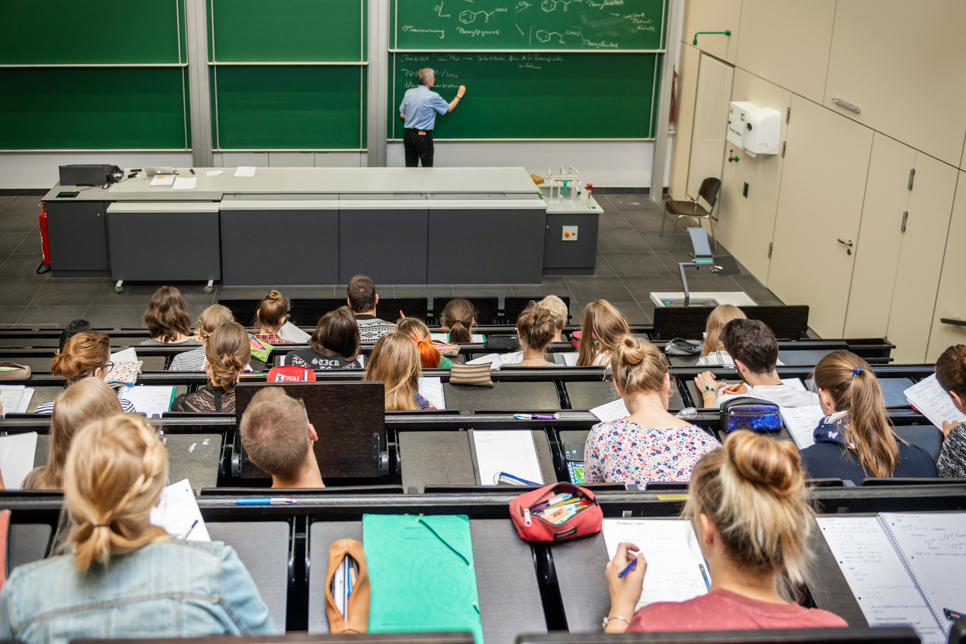 A lecturer is giving a lecture in a large auditorium with full of students.