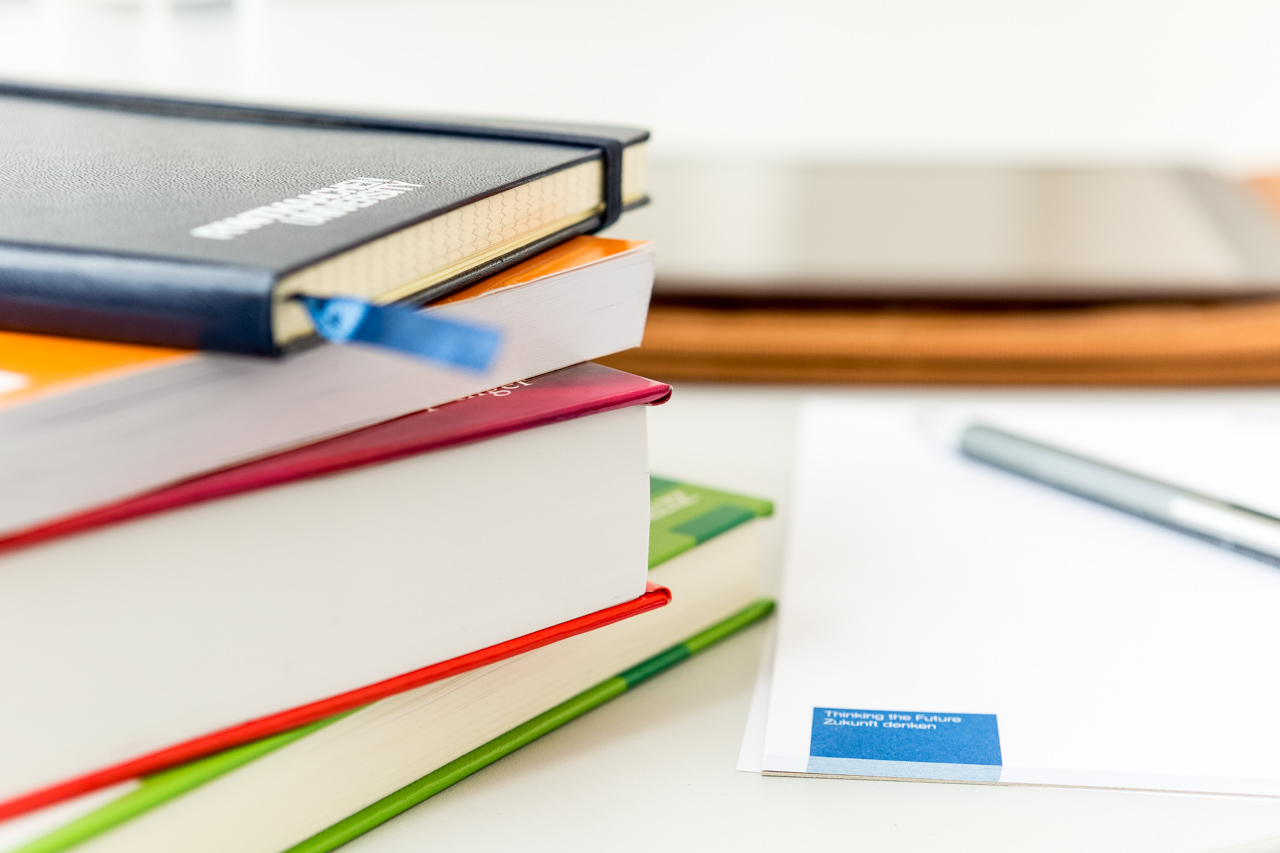 A block of  four  books and a notebook with a pen on it are shown.